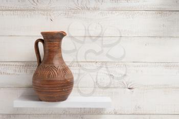 clay jug at shelf on white wooden plank background