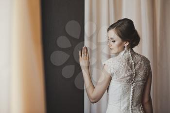 Girl in a wedding dress stands near the curtains.