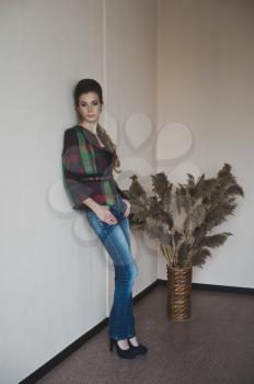 Beautiful girl stands near the chairs and the vase with reeds.