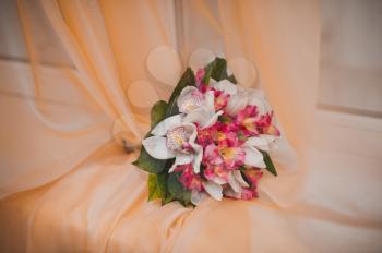 The bouquet for the bride lies on an orange curtain on a window sill.