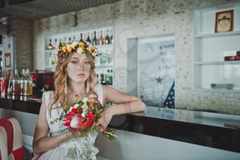 Beautiful girl with bouquet of flowers and a wreath of them.