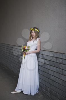Portrait of a girl in a white dress against the wall.