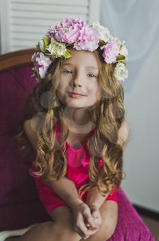 Little girl in a wreath of lilac flowers sitting on the sofa.