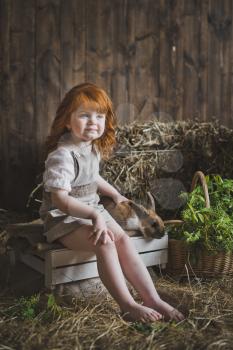 The child is sitting on the boxes among the hay.