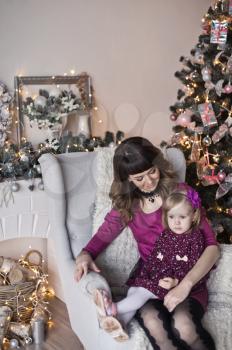 Portrait of baby and mother sitting on a chair near the Christmas tree.