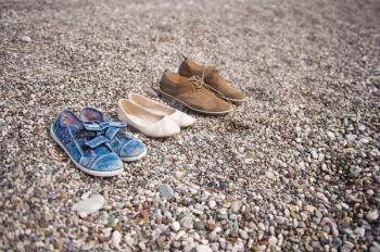 Different pairs of shoes on the pebbled shore.