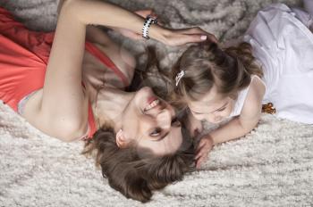 Mother and daughter lying with their heads towards each other on the bed.