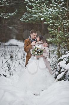 A young couple stands against a snowy pine forest.