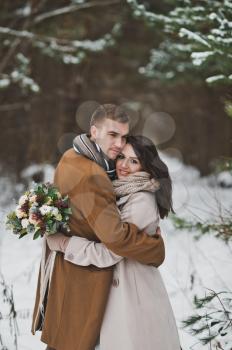 Strong gentle embrace of the newlyweds on background of a winter forest.