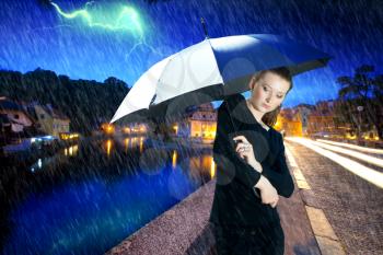 girl under an umbrella during a thunderstorm in the evening in the summer in a small European town. weather forecast