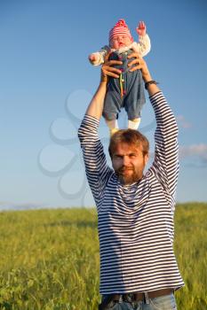 baby in funny clothes standing on his head with his father and waves