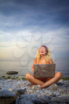 girl laughs looking at a laptop on the beach