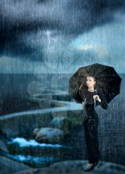 beautiful girl sitting on the bank of the dam at the sea during a storm under the umbrella. lightning comes rain