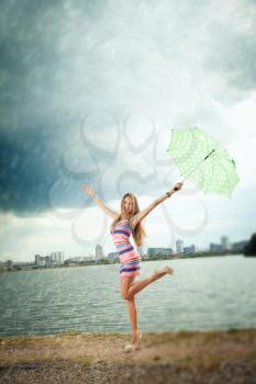 happy girl under an umbrella walks in the rain during the summer along the river against the background of the city