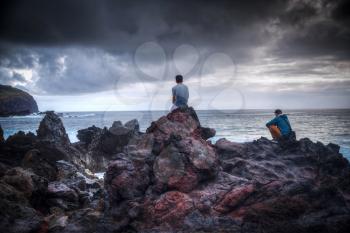 Two men sit on the rocks and watch the Easter Island on the ocean