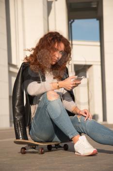 girl looking into the phone, listening to music sitting on the skateboard