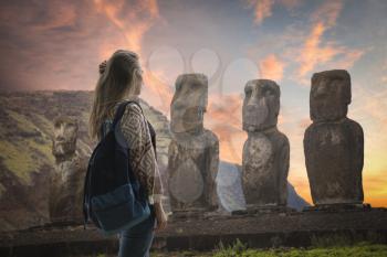 girl tourist with a backpack looking at the statues of Easter Island