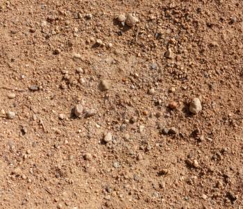 Ground textured surface background under bright sunlight, sandy soil close-up macro view