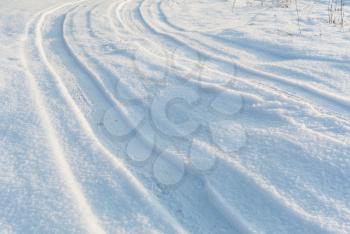 Country road on snow field under day sunlight, car tire tracks on white winter snow, perspective view, white winter landscape