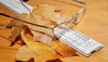 Glasses, ruler and chalk with yellow maple leaves on a wooden background