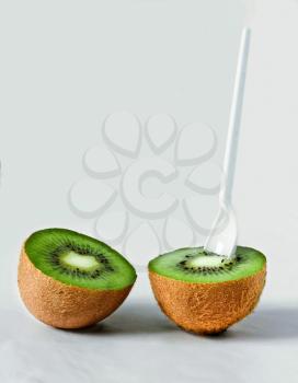 Two halves of kiwi with a spoon and a straw on a light background