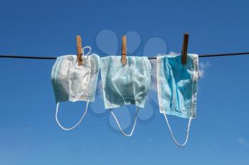 Three used washing face masks drying against a blue sky on a sunny day
