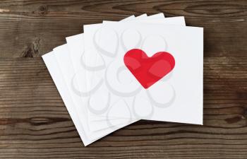 Stack of white square paper cards with hearts on old wooden background. Envelopes with hearts. Top view.