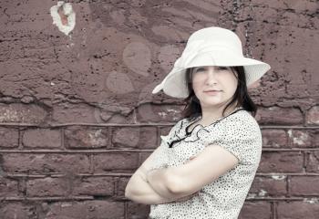 Vintage portrait of pretty young woman against brick wall background. Woman in white hat. Toned photo with copy space. Vintage style photo.