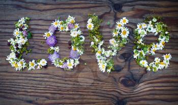 Inscription LOVE made of flowers and leaves on vintage wooden table background. Word love made of flowers.Top view.