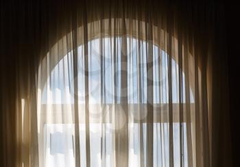 Transparent curtains on the window with arch. Sunlight streaming through the window with a transparent curtain.