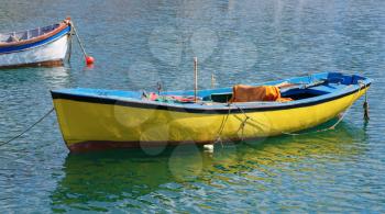Old fishing rowing boat painted in yellow on the water on a sunny summer day.