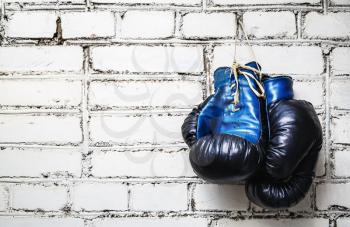 Pair of old blue and black boxing gloves hanging on white brick wall.