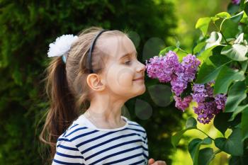 Little girl child smelling lilac flowers in the garden. Selective focus.