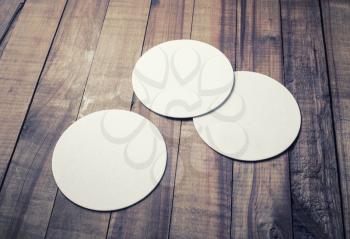 Three blank white beer coasters on wooden background. Responsive design mockup.
