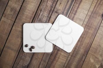 Two blank square beer coasters and coffee beans on wood table background. Flat lay.