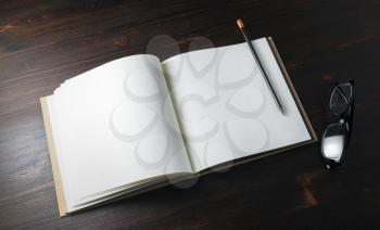 Opened book with blank paper pages, pencil and glasses on wooden background.
