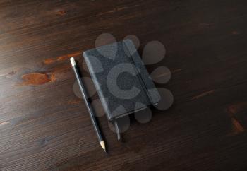 Photo of black notepad and pencil on wood table background.