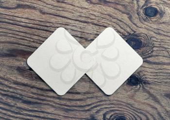 Photo of two blank white beer coasters on wood table background. Blank template for your design. Top view. Flat lay.