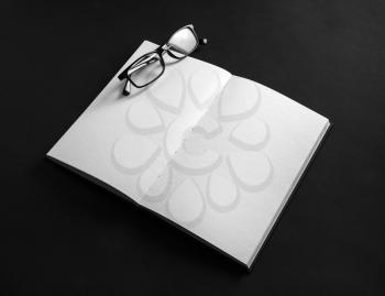 Opened blank book and glasses on black background.