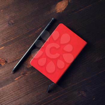 Red notepad and pencil on dark wood table background. Flat lay.