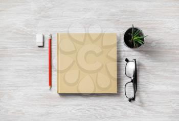 Closed book and blank stationery: glasses, pencil, eraser and plant on light wood table background. Top view. Flat lay.