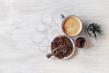 Delicious fresh coffee. Coffee cup, coffee beans, plant and ground powder on light wood table background. Copy space for your text. Flat lay.