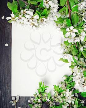 Blank paper poster and spring flowers on wooden background. Vertical shot. Flat lay.