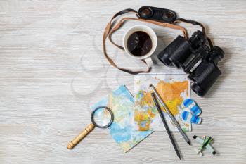 Travel plan background. Map, binoculars, magnifier, pencils, coffee cup, airplane and flip flops on light wooden background. Top view. Flat lay.