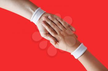 Helping hands concept. Female hands with white bracelets on red backgroung.
