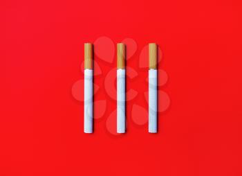 Three cigarettes on red background. Flat lay.