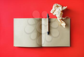 Photo of kraft open book with blank pages, crumpled paper and pen on red paper background. Mockup for placing your design. Top view. Flat lay.
