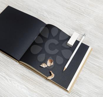 Photo of blank black notebook, pencil and eraser on light wooden background.