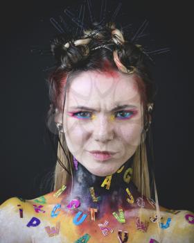 Emotional portrait of a young girl with creative makeup and colorful letters on her shoulders