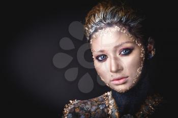 Portrait of a blue eyed young girl with creative golden makeup in the style of icon painting isolated on black background